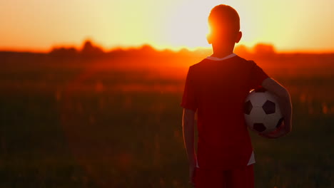 boy-with-a-ball-in-a-field-at-sunset-boy-dreams-of-becoming-a-soccer-player-boy-goes-to-the-field-with-the-ball-at-sunset.